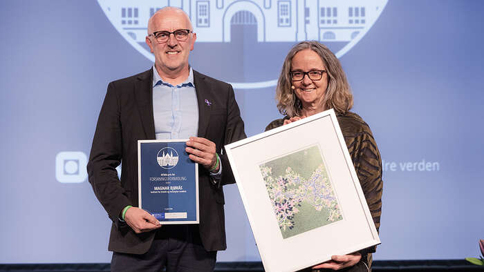 Magnar Bjørås på scenen der han mottar diplom og kunst fra prorektor Monica Rolfsen